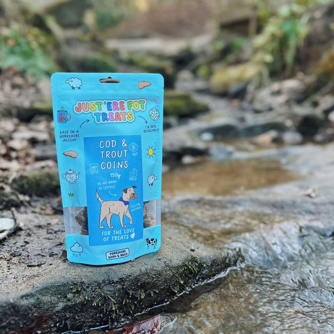 Front view of a packet/ pouch of 'Just'ere for treats' natural cod and trout coins on a wet riverbed background