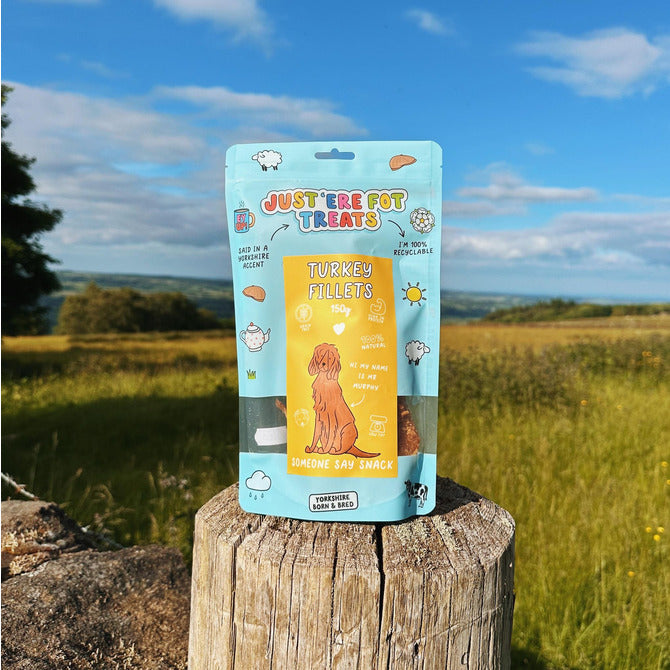 Front view of a packet/ pouch of just'ere for treats Turkey Fillets on a old fence post with feild and trees in the background
